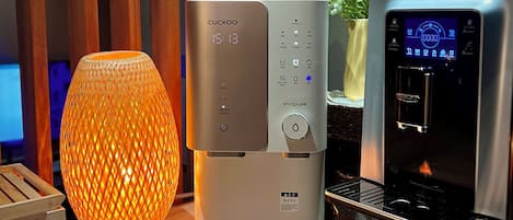Una cocina moderna con una cafetera Cuckoo, una máquina de espresso Teatime y una lámpara naranja decorativa.