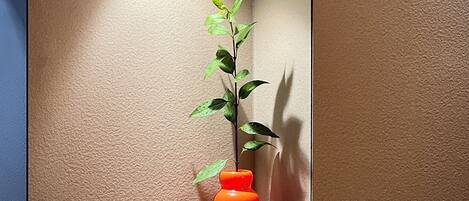 A corner with a textured wall, a reflective surface, and a plant in a unique orange vase.