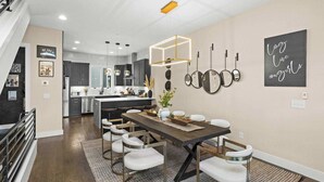 A modern kitchen with a central island, stainless steel appliances, and a dining area with a wooden table and white chairs. - Luxury Nashville - Rooftop, FireTable & City Views (Nashville)