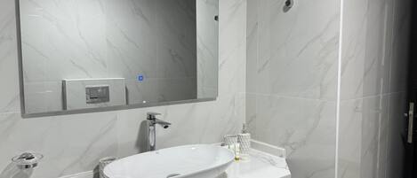 Une salle de bain avec un grand miroir, un lavabo blanc et un mur recouvert de carreaux de marbre.