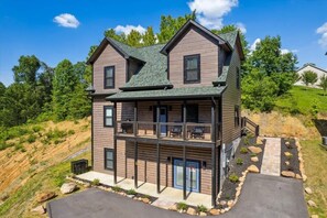 Une cabane en rondins à deux étages, dotée d’un balcon au niveau supérieur, entourée d’un jardin aménagé et située au pied d’une colline.