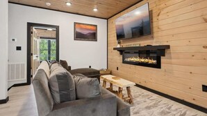 A modern living room with a large gray sofa, a wooden coffee table, and a fireplace. - Villa De Luxe by Beyond Expectations: Cabin w/ Indoor Pool, Hot Tub & Game Room (Pigeon Forge)