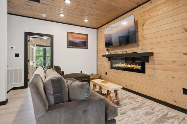 A modern living room with a large gray sofa, a wooden coffee table, and a fireplace. - Villa De Luxe by Beyond Expectations: Cabin w/ Indoor Pool, Hot Tub & Game Room (Pigeon Forge)