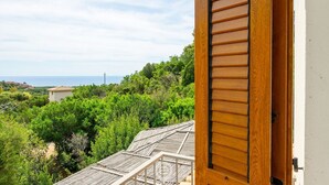 A wooden door with a view of a lush green landscape and a distant building. - Simone’s Eden Apartment (Eden Rock)