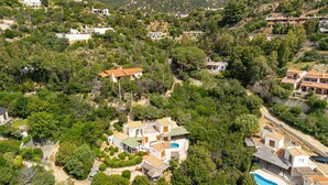 An aerial view of a hillside residential area with multiple houses, a swimming pool, and lush greenery. - Simone’s Eden Apartment (Eden Rock)