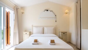 A hotel room with a large bed, two bedside tables, a window with curtains, and a wall-mounted light fixture. - Simone’s Eden Apartment (Eden Rock)