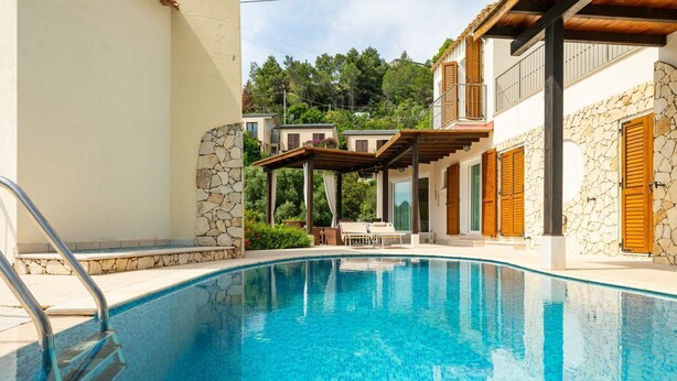 A swimming pool with a stone wall and wooden shutters, surrounded by a covered patio and a stone staircase. - Simone’s Eden Apartment (Eden Rock)