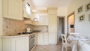 A kitchen with white cabinetry, a stove, and a dining area with a table and chairs. - Simone’s Eden Apartment (Eden Rock)