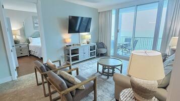 Habitación de hotel con cama, televisión, zona de estar con mesa y sillas, y balcón con vistas.