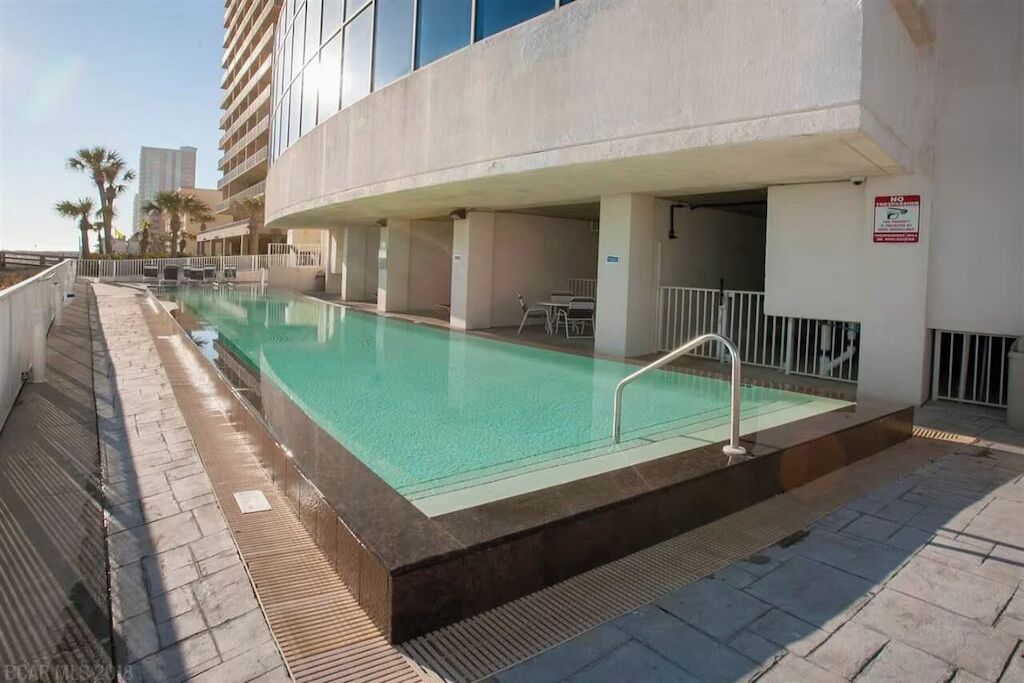 A swimming pool with a safety railing, adjacent to a building with a white facade and a sign indicating a no parking zone.