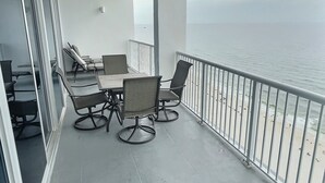 Een balkon met een tafel en stoelen, met uitzicht op een strand.
