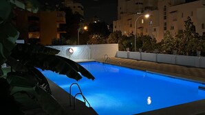 Une piscine avec un escalier, entourée d’un petit muret et agrémentée de plantes en pot.