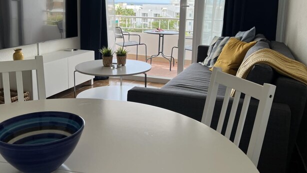 Un salon moderne doté d’un téléviseur à écran plat, d’une table de salle à manger ronde, d’un canapé et d’un balcon offrant une vue sur la ville.