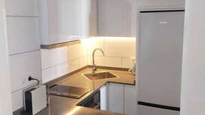 Une cuisine compacte avec des meubles blancs, un évier en acier inoxydable et un four encastré.