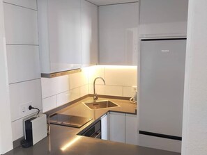 A compact kitchen with white cabinets, a stainless steel sink, and a built-in oven.