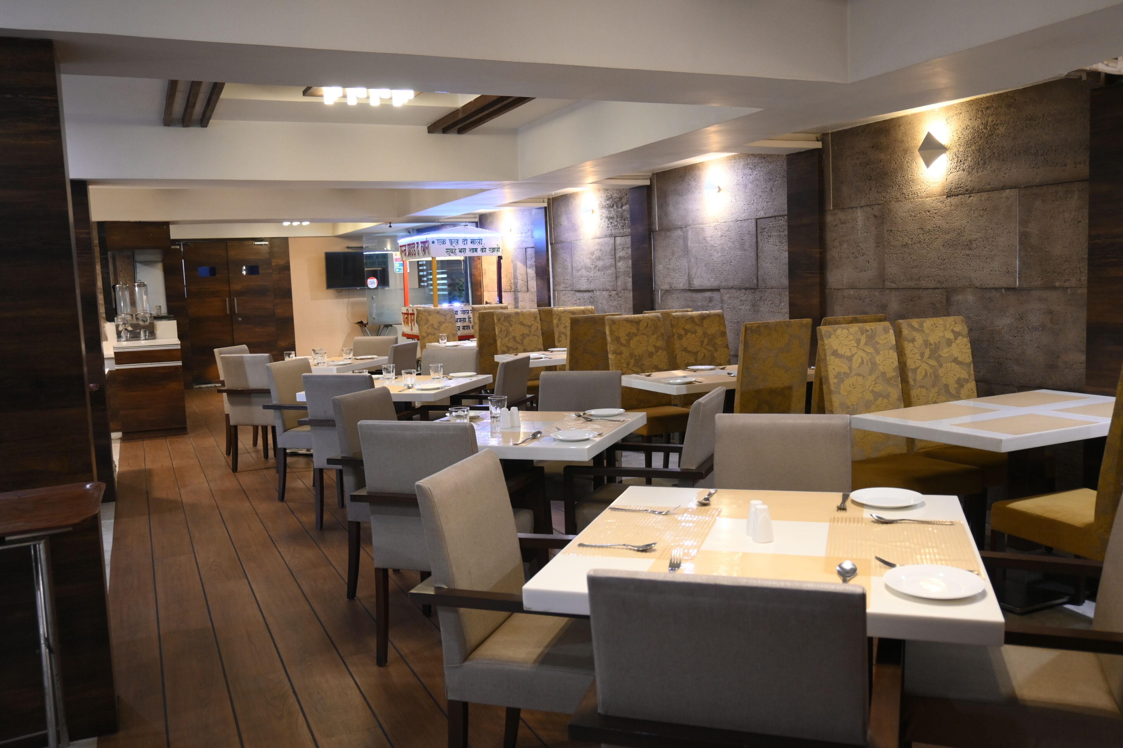 Restaurante com várias mesas e cadeiras, piso de madeira e parede de pedra.