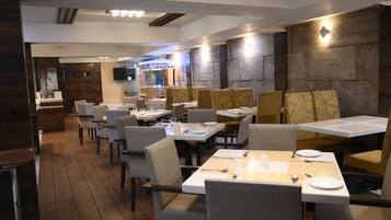 A restaurant with multiple tables and chairs, wooden flooring, and a stone wall.