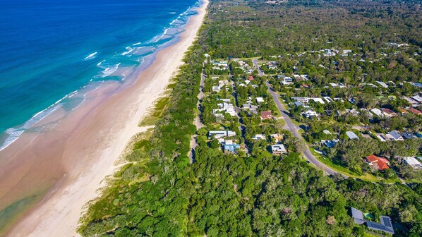 Vue aérienne d’une zone résidentielle côtière, avec des maisons, une plage et une végétation luxuriante.