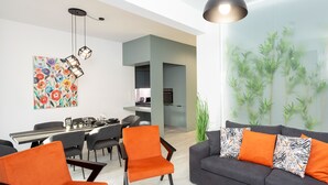 Un salon moderne avec un canapé gris, des fauteuils orange et un coin repas comprenant une table et des chaises.