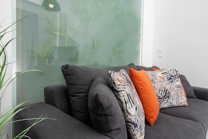 Een moderne woonkamer met een grijze bank, twee gestreepte kussens en een groene plant.