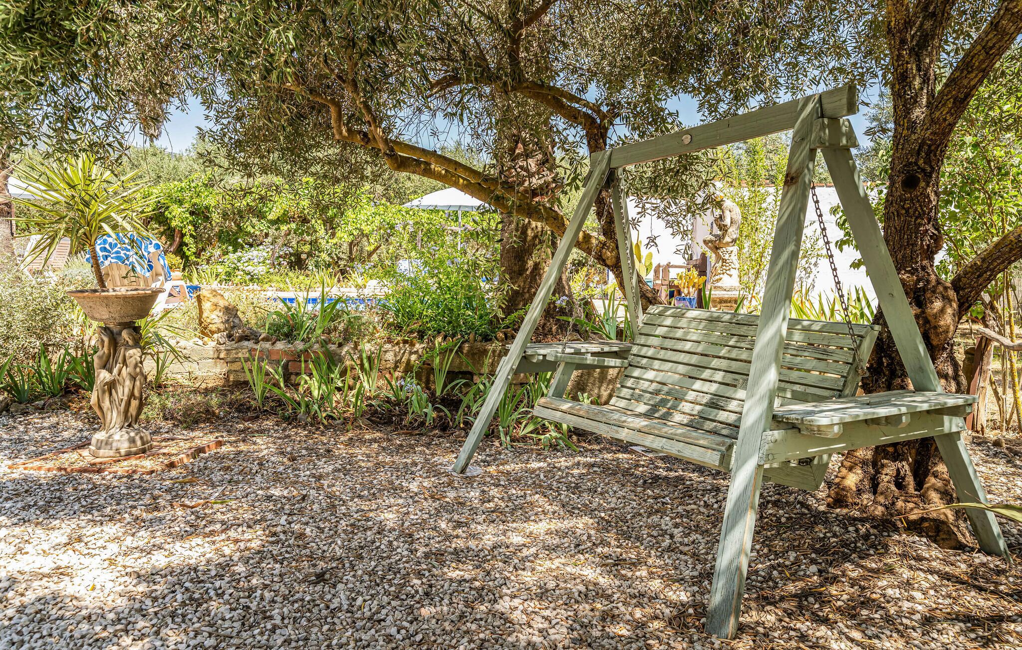 A wooden swing under a tree in a garden with pebbles on the ground.