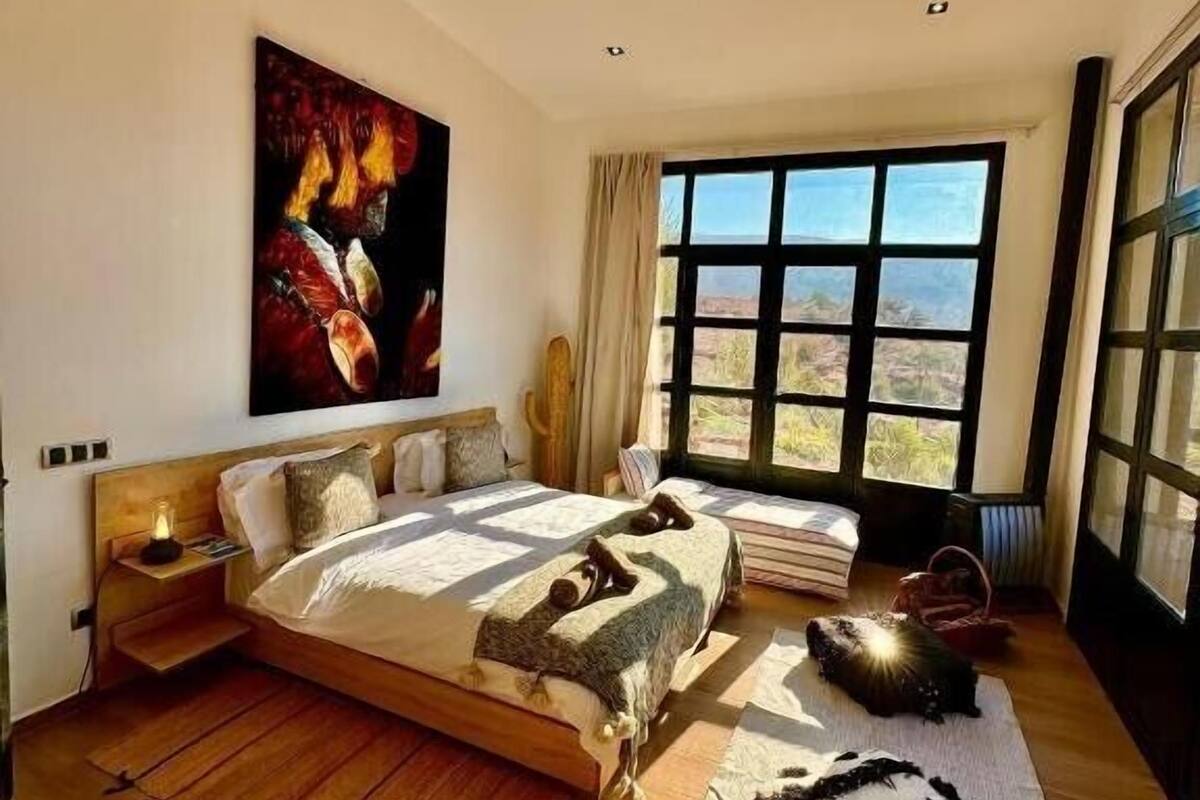 A spacious bedroom with a large bed, a view of the desert through a large window, and a painting on the wall.