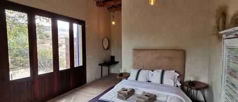 Une chambre spacieuse avec un grand lit, un plafond en bois et une vue sur l’extérieur grâce à une grande fenêtre.