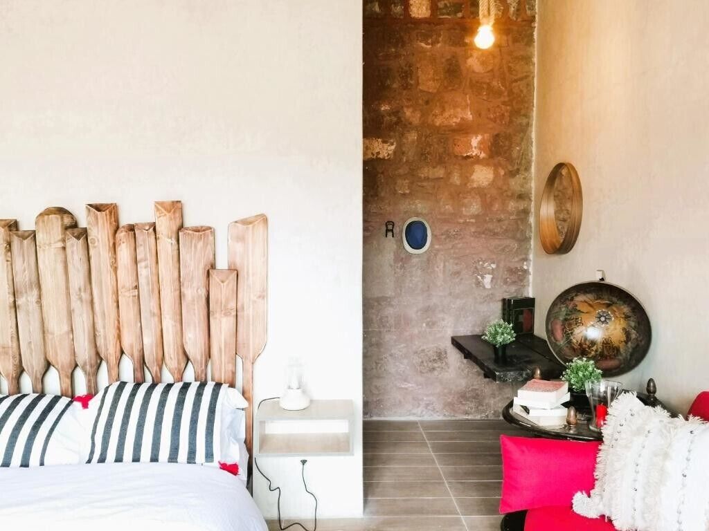 A bedroom with a wooden headboard, a bed with striped bedding, a small bedside table with a lamp, and a red accent wall.