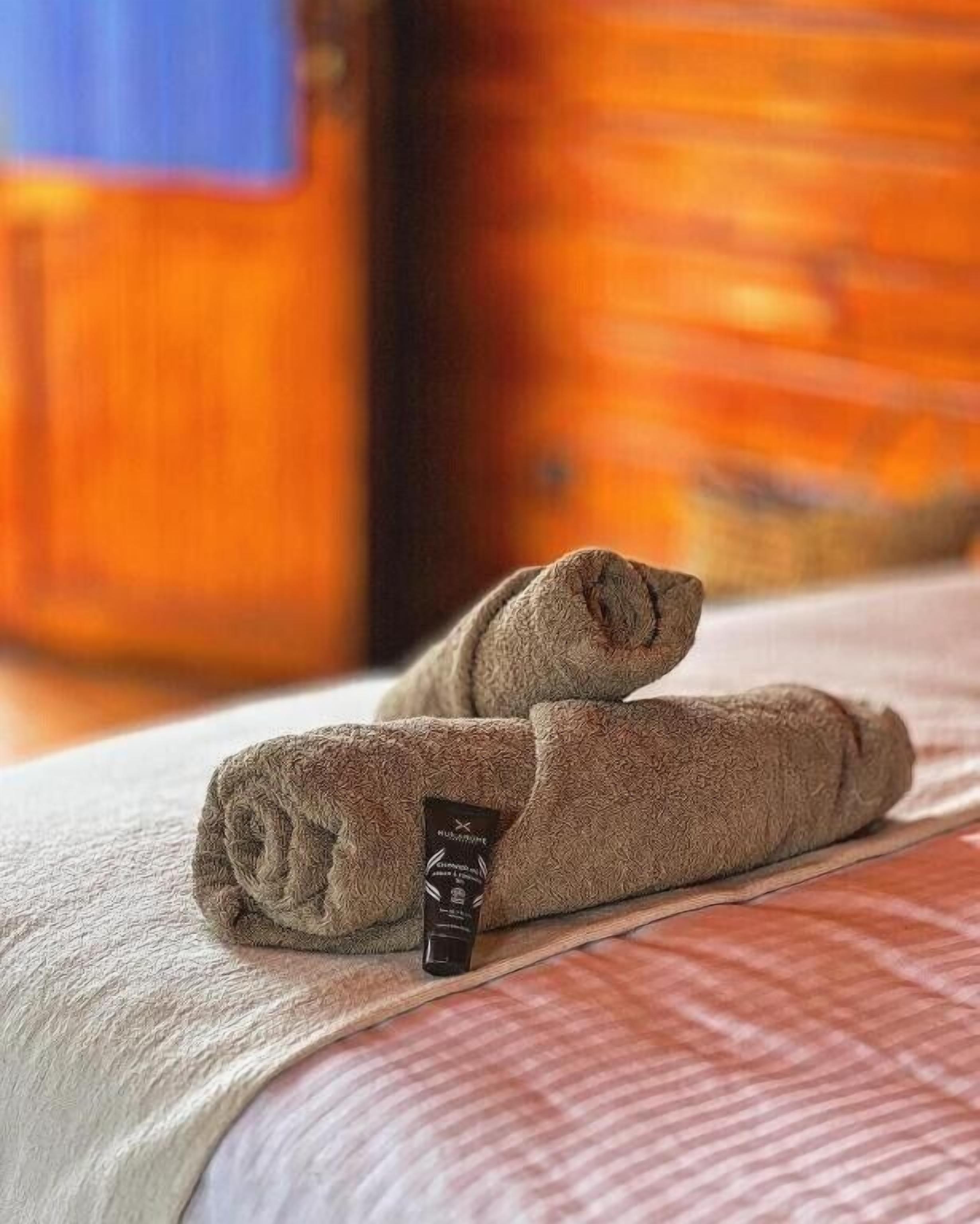 Une serviette soigneusement pliée, ornée d’une étiquette noire, est posée sur un lit recouvert d’une couvre-lit à rayures.