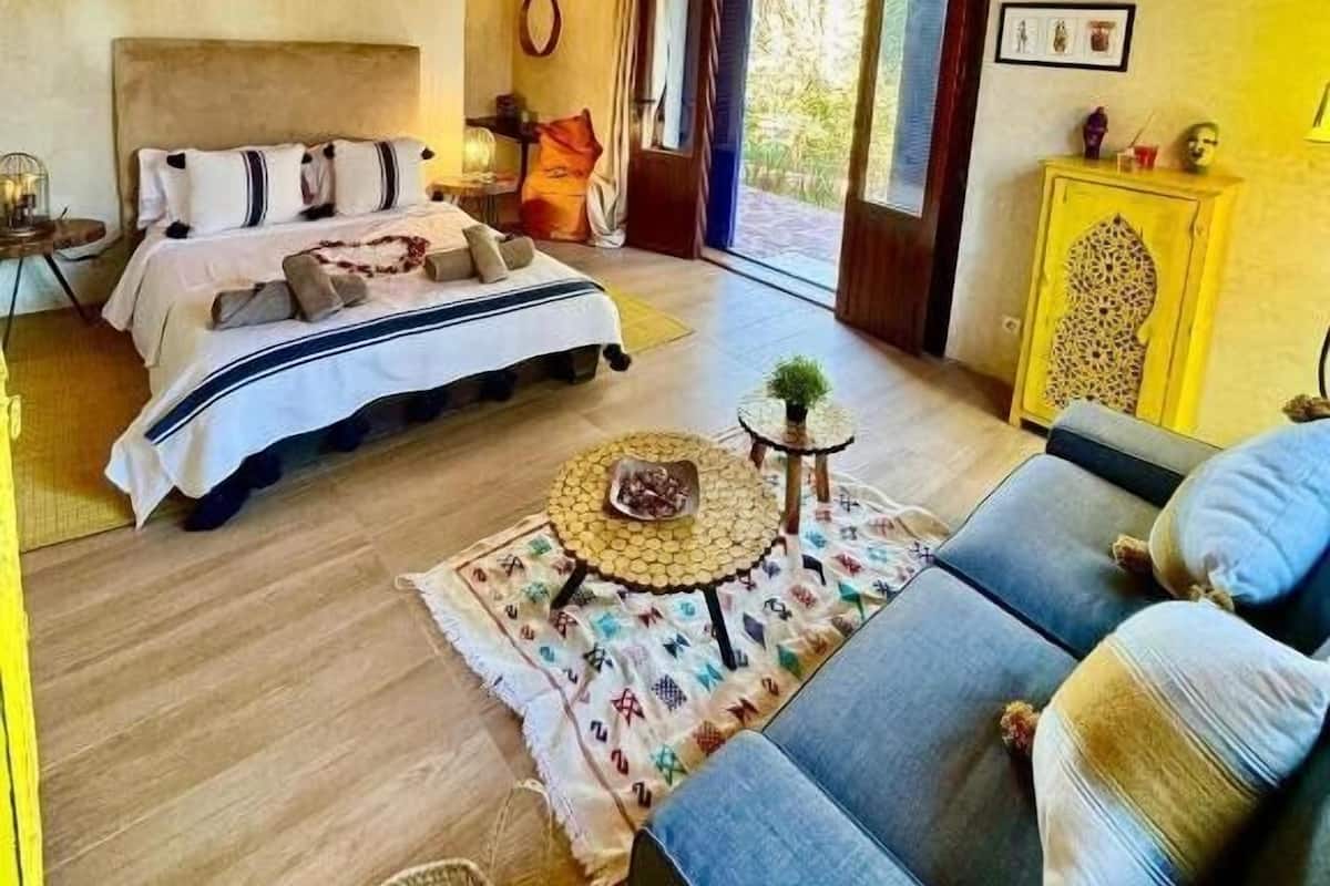 A cozy bedroom with a bed, a sofa, a small table, and a yellow cabinet.