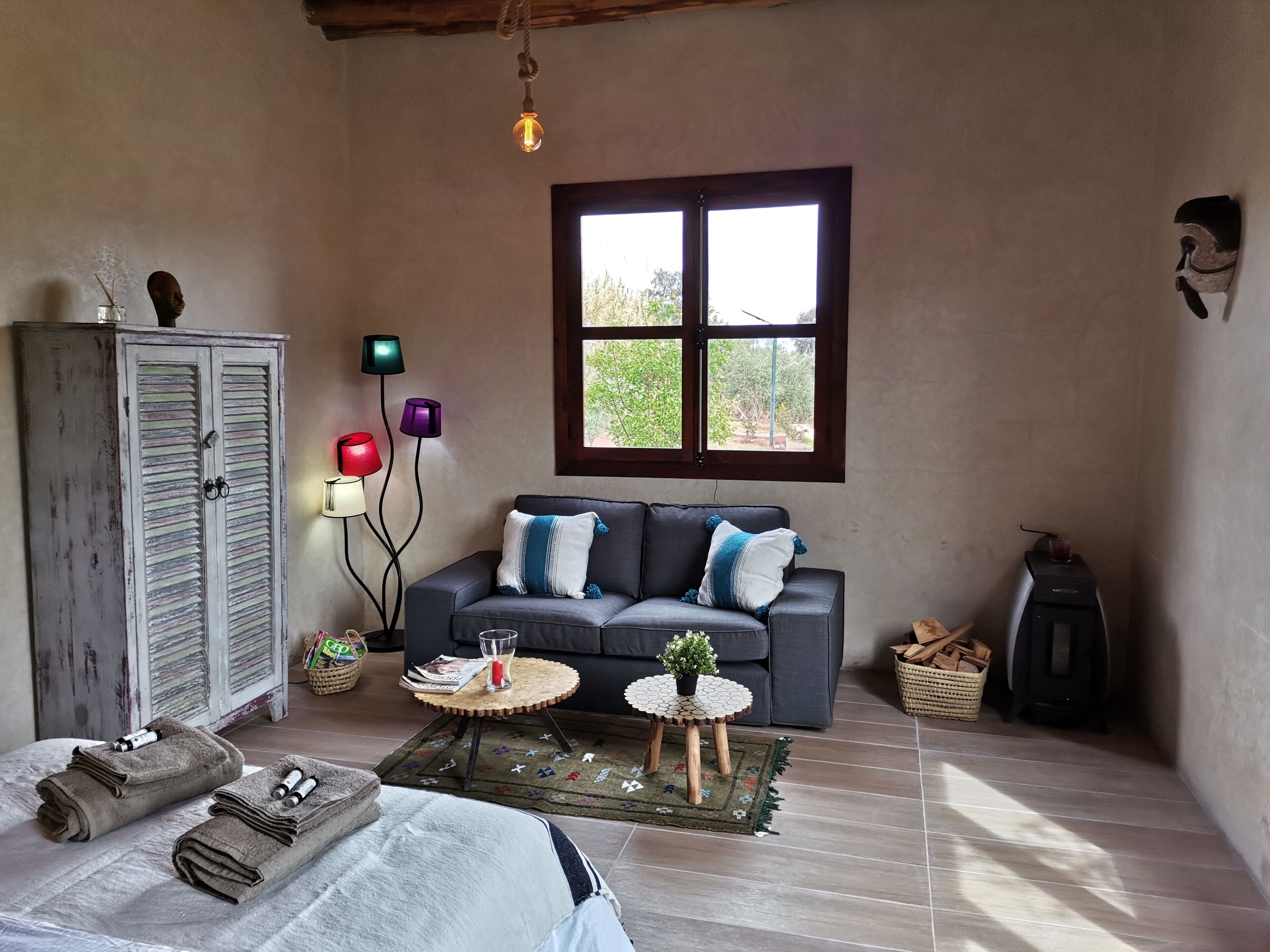 A cozy room with a grey sofa, a wooden cabinet, a window with a view, and a small table with a plant.