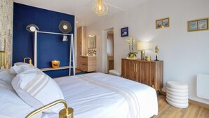 A bedroom with a large bed, a wooden wardrobe, a mirror, and a blue accent wall. - Maison agréable près Etretat (Beaurepaire)