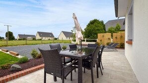 A patio with wicker furniture and a glass table, surrounded by a brick border and a gravel area. - Maison agréable près Etretat (Beaurepaire)