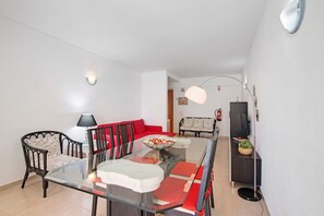 A modern living room with a glass dining table, red and black chairs, a red sofa, and a television on a stand. - Gabriel 6 H Apartment with Shared Pool, Balcony and Air Conditioning (Armação de Pêra)
