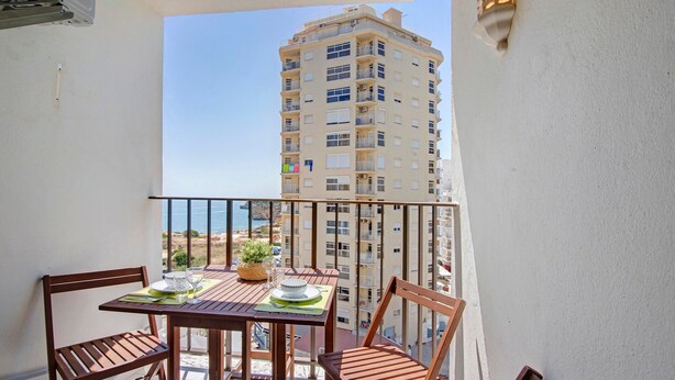 Un balcon avec une table et des chaises, un pot de fleurs et une vue sur un immeuble de grande hauteur.