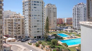 Un immeuble résidentiel de grande hauteur doté de nombreux balcons, d’une piscine et d’un petit espace vert aménagé avec des chaises longues.