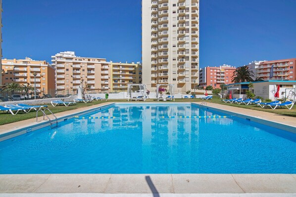 A swimming pool with lounge chairs, surrounded by high-rise buildings. - Gabriel 6 H Apartment with Shared Pool, Balcony and Air Conditioning (Armação de Pêra)