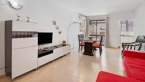 Un salon moderne doté d’un téléviseur à écran plat, de meubles blancs, d’un coin repas avec une table en verre et d’un canapé rouge.