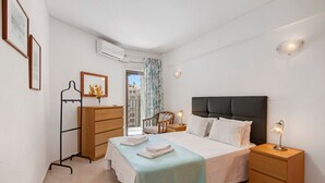 Une chambre à coucher comprenant un lit, des tables de chevet, une armoire, une chaise et une vue sur l’extérieur.