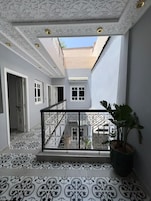 Un patio con techo ornamentado y baldosas de suelo con diseños, una planta en maceta y una escalera que conduce a un nivel superior.