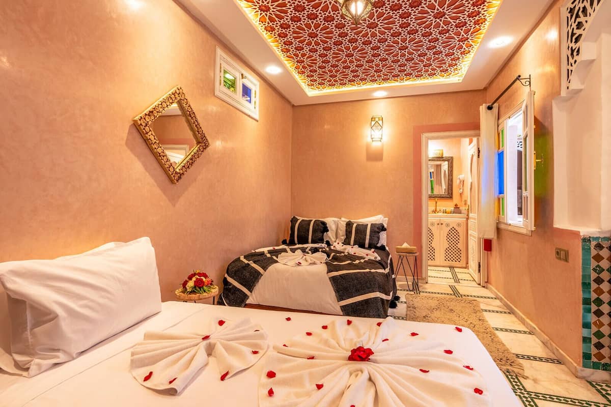 A hotel room with a bed, a mirror, a small table with flowers, and a decorative ceiling.