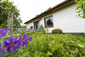 A white house with a wooden roof, large windows, and a garden with purple flowers. - Holiday Home 'Ferienhaus Schober' with Private Terrace, Garden and Wi-Fi (Cuxhaven)