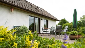 A house with a patio, a dining table with chairs, a green umbrella, and a potted plant.