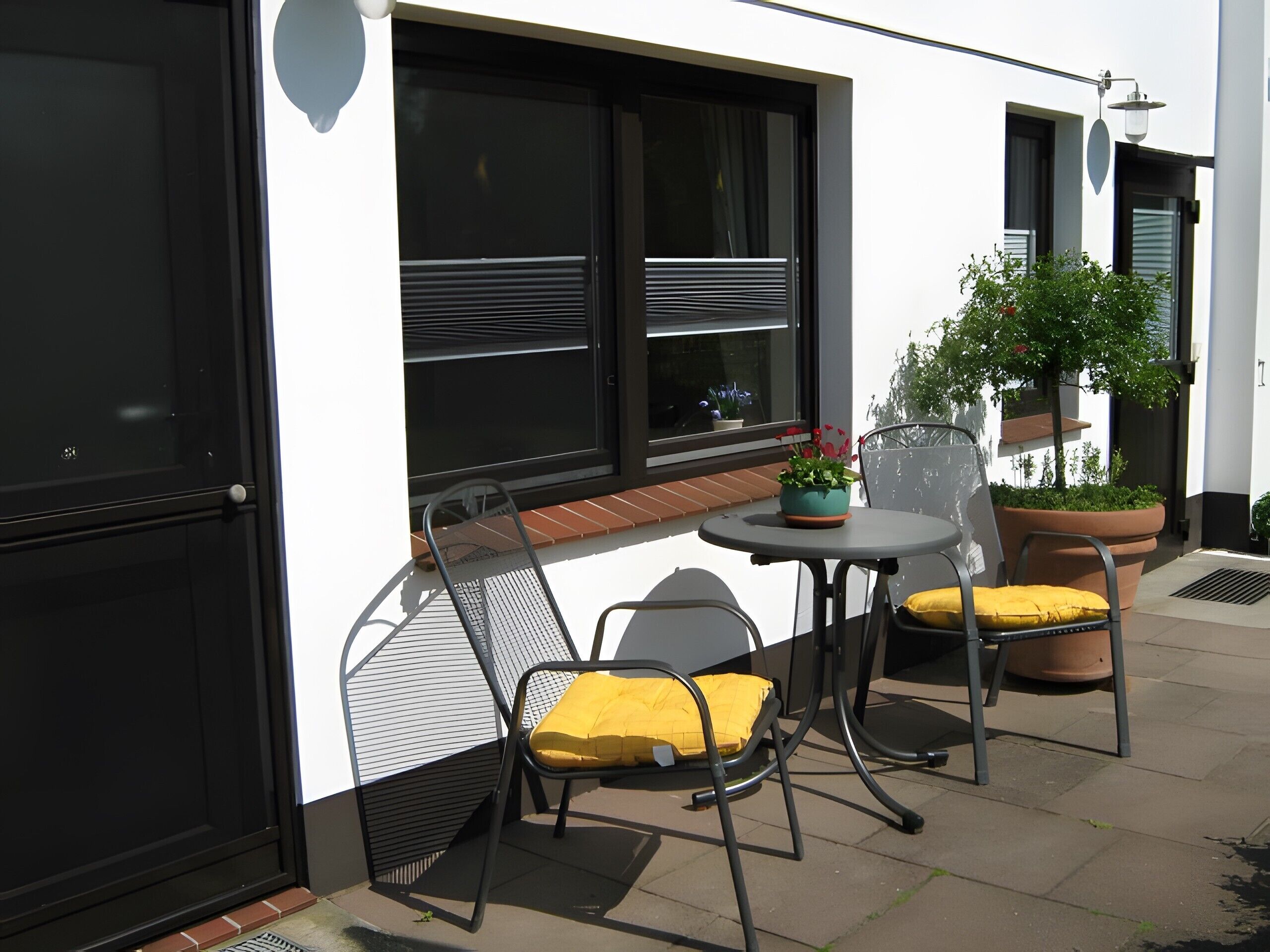 A patio with a table and two chairs, a potted plant, and a window with blinds.