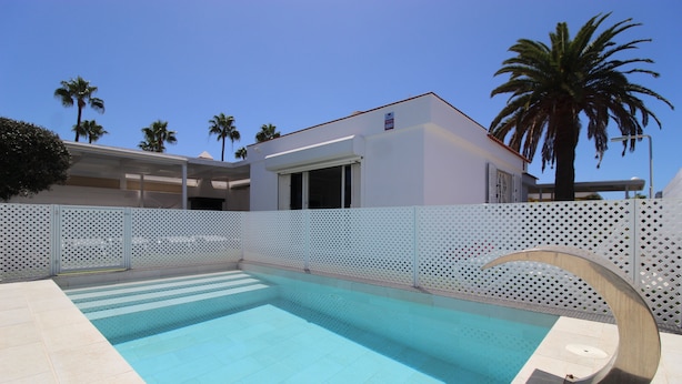 Una piscina con valla blanca, palmeras y un edificio moderno al fondo.