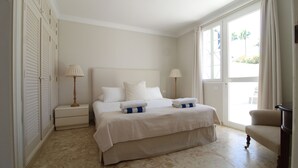 Habitación de hotel con una cama grande, dos mesitas de noche con lámparas, una silla y vistas al exterior a través de un ventanal amplio.