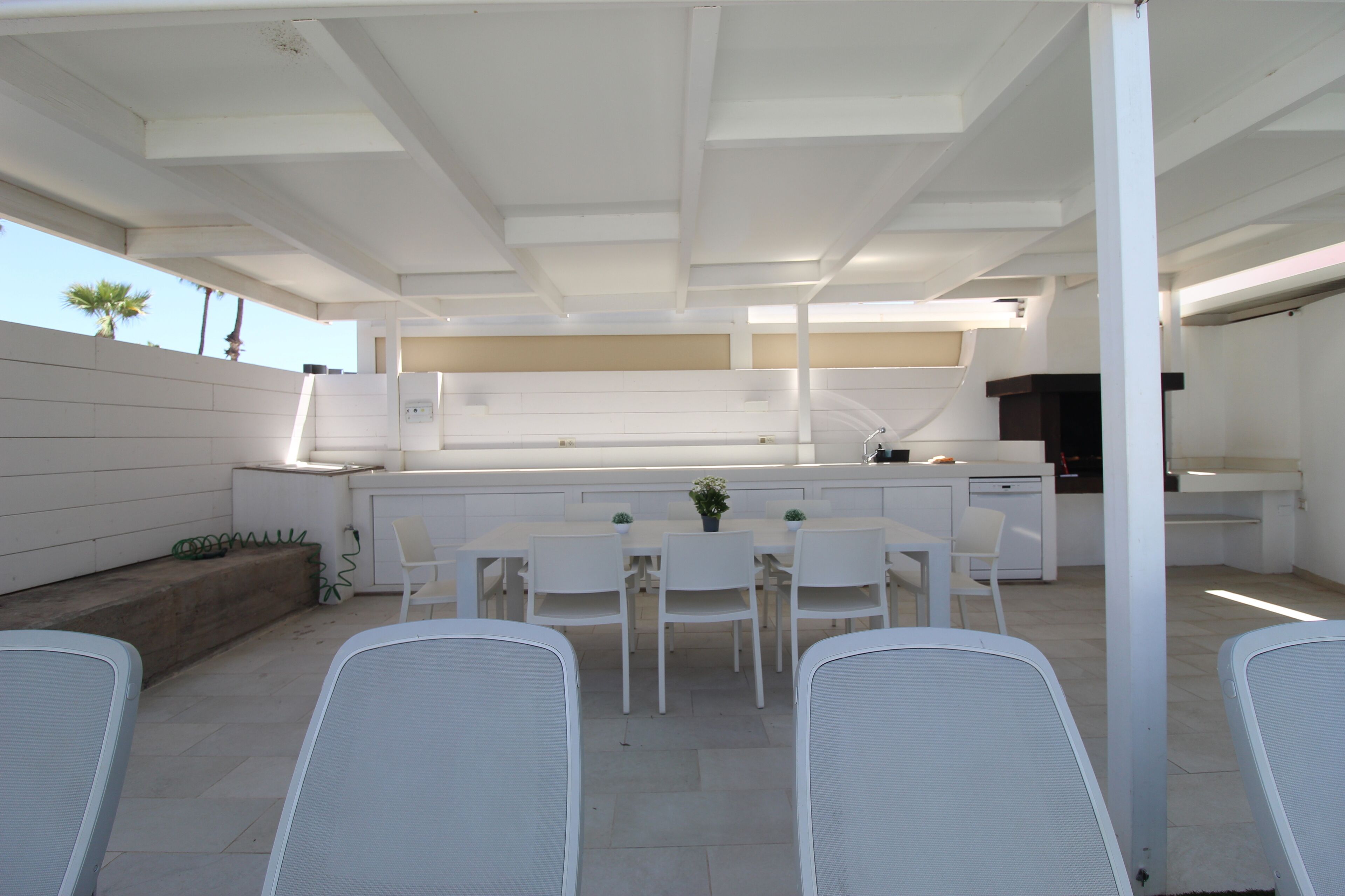 A modern outdoor kitchen with white furniture and a dining area.