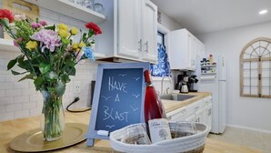 Eine Küche mit weißen Schränken, einer Tafel mit der Aufschrift 'HAVE A BLAST', einer Blumenvase und einer Weinflasche.