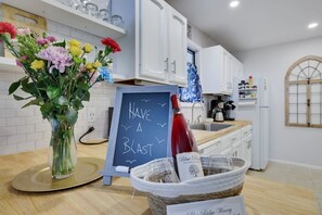 Una cucina con mobili bianchi, una lavagna con la scritta 'HAVE A BLAST', un vaso con fiori e una bottiglia di vino.