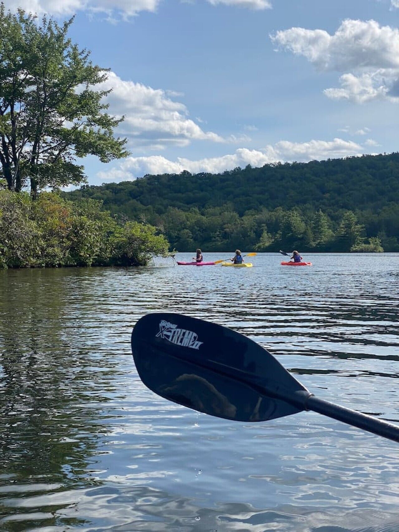 A calm lake with kayaks and a paddle in the foreground.